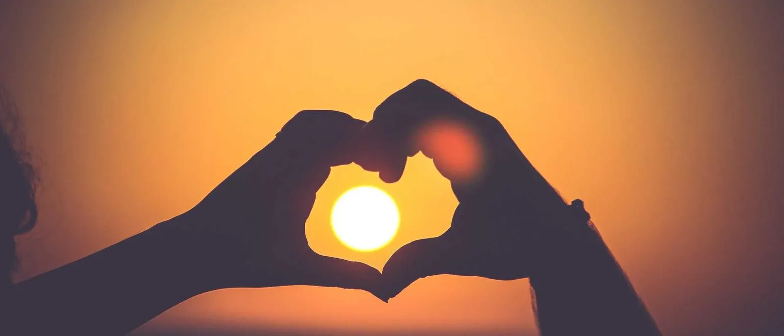 Zwei Hände formen ein Herz vor der untergehenden Sonne